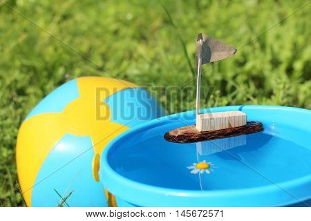 Children's homemade toy ship in a bucket full of water on a background of grass and ball / imaginary outdoor recreation in summer