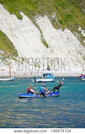LULWORTH COVE, UNITED KINGDOM - JULY 19, 2016 - Holidaymakers and their dog in an inflatable boat with the beach to the rear Lulworth Cove Dorset England UK Western Europe, July 19, 2016.
