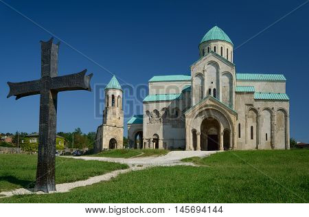 Cathedral of the Dormition or Kutaisi Cathedral more commonly known as Bagrati Cathedral against blue sky background. Bronze cross in foreground.