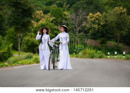 Two girls in Vietnamese's traditional costumes - Long-dress (the Ao dai - Vietnamese) - and Royal Poinciana road (Delonix Regia). The charming beauty of Vietnam women.