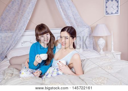 Mother And Daughter Lay In Bed And Drinking Tea.
