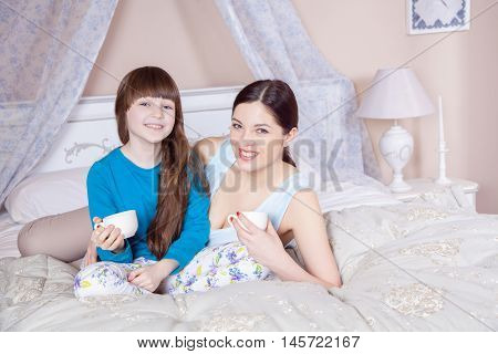 Mother And Daughter Lay In Bed And Drinking Tea.