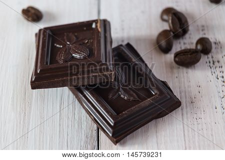 Two pieces of dark chocolate and coffee beans on a wooden table