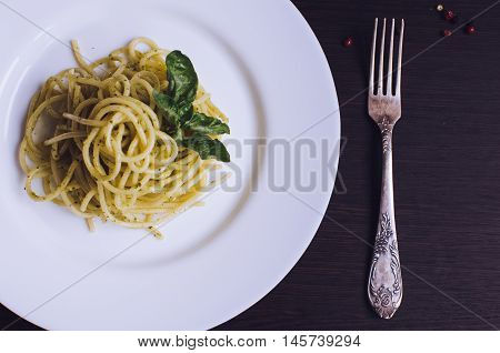 Close up italian pasta spaghetti with homemade green pesto sauce and basil leaf with a fork on dark background. Delicious healthy vegetarian food. Italian food concept. Top view.