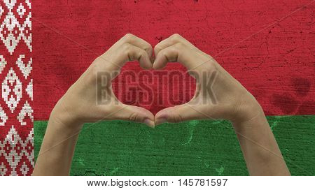 With a stylized Belarusian flag background an anonymous person's hands being held in the form of a heart, symbolizing love and patriotism for Belarus.