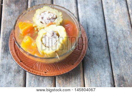 Stuffed bitter gourd with minced pork in clear soup sereved in glass bowl on wooden background.