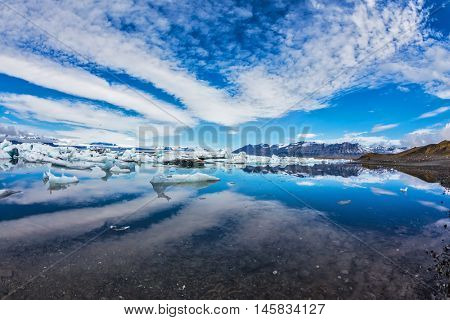 Ice lagoon in Iceland. Beautiful summer morning in the ocean bay with ice floes. Stratus, diverging fan, reflected in the mirrored surface of the water