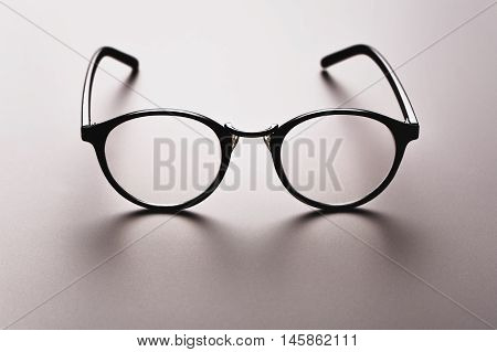 Black satine plastic circle eye glasses for womenor hipster, lying on grey background with accurate shadow.