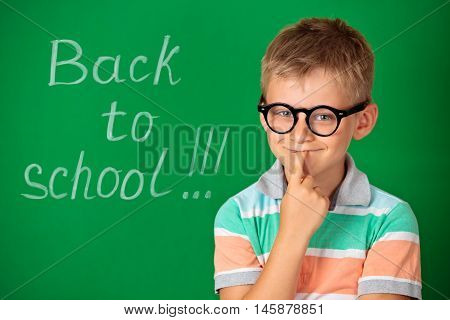Education and school concept . Schoolboy wearing glasses against green chalkboard.