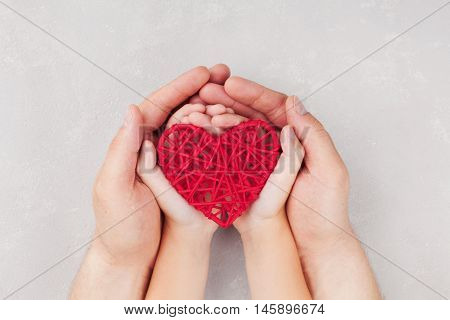 Adult and child holding red heart in hands top view. Family relationships health care pediatric cardiology concept.