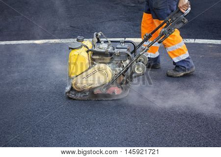 Worker use vibratory plate compactor compacting asphalt at road repair