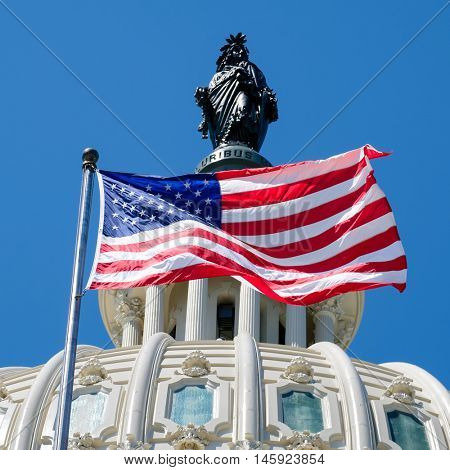 The US National Flag waves in fron of the Capitol building dome featuring the Statue of Freedom in Washington D.C.