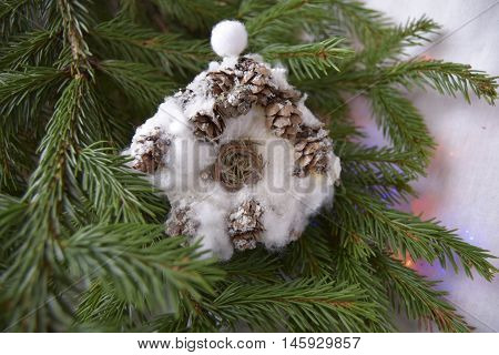 Christmas toy in the form of the house. The toy is located on a fir-tree. The house is made of fir cones and cotton