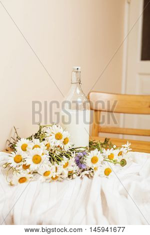 Simply stylish wooden kitchen with bottle of milk and glass on table, summer flowers camomile, healthy foog moring concept noone