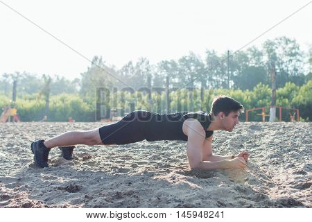 Fit man doing pank exercise during training workout on beach in summer