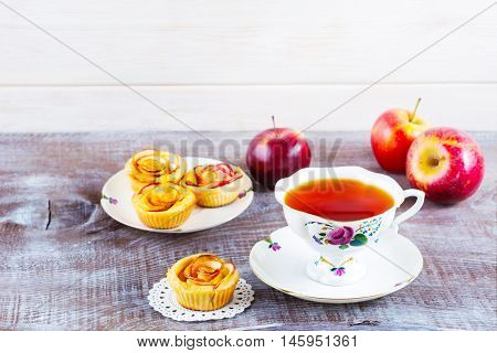 Cup of tea and apple roses shaped muffins on rustic wooden table. Sweet apple dessert pie. Homemade apple rose pastry. Breakfast tea with sweet apple pastry