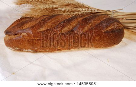 bunch of mown wheat ears with vintage handmade reaper hook sickle and rye dark white french fresh bread loaf on light linen tablecloth