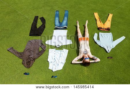 Fashion man lies undressed on greed grass background with his clothes allocated like in wardrobe