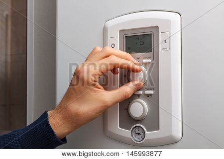 Men hand regulate high temperature on 75 degree in control panel of central heating.