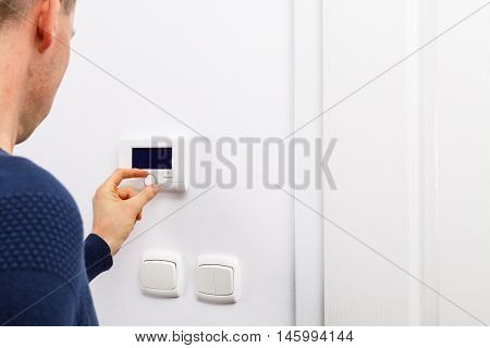 Men regulate temperature on control panel of central heating at wall in living room.