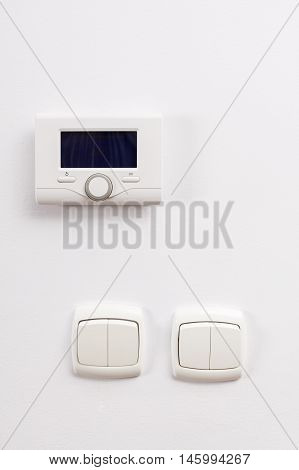 Control panel of central heating and two light switch at white wall on living room.