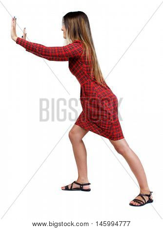 back view of woman pushes wall. Isolated over white background. girl in red plaid dress stands sideways and pushing his hands something to the side.
