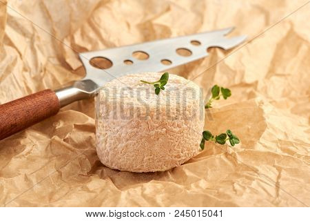 Crottin Cheese With Thyme Leaves And A Knife On A Brown Package Paper.