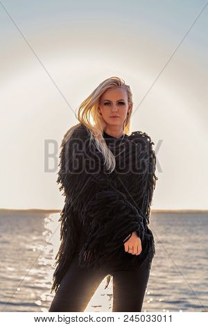 Attractive Cutie Blond Smiling Girl Shivering From The Wind In A Fur Coat At Sunset On The Beach