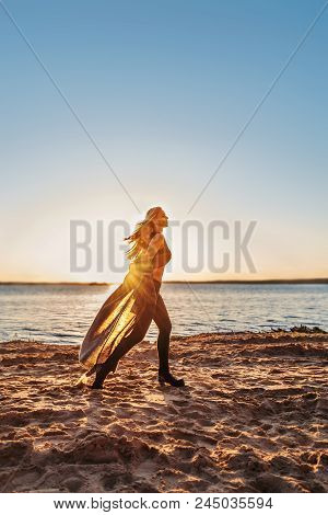 Young Blond Girl With Fluttering Hair And Clothes Running Along The Beach In Bright Highlights Glare