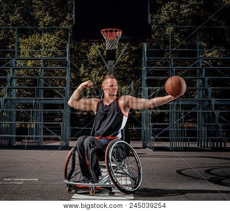 Strong Basketball Player In A Wheelchair Pose With A Ball On Open Gaming Ground.