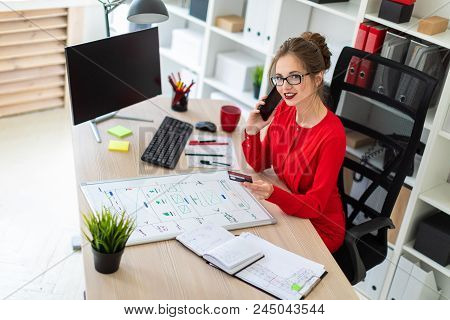 Beautiful Young Girl In Glasses And A Red Shirt Is Working In The Office. Photo With Depth Of Field.
