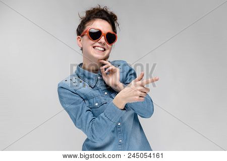 Young Girl With Glasses In Heart On Gray Background. Portrait Of A Young Beautiful Girl. Charming Gi
