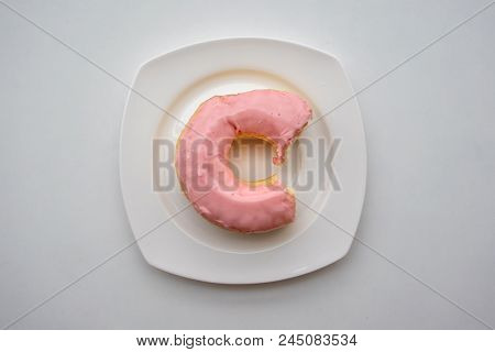 Bite Donut Ring With Strawberry Flavor Glaze Frosting On White Plate Against White Background.