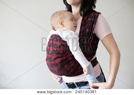 A Cropped View Of A Baby In A Woven Wrap. A Babywearing Mother Carrying Her Sleeping Child In A Slin