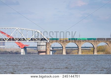 A Freight Train Is Driving Across A Bridge Across The River