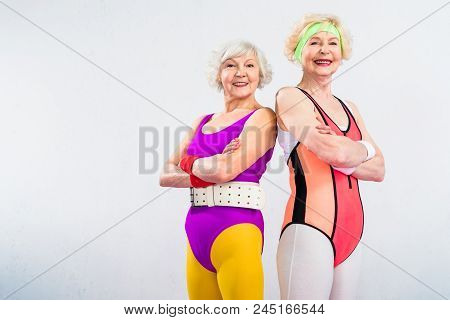 Happy Senior Sportswomen Standing With Crossed Arms And Smiling At Camera Isolated On Grey