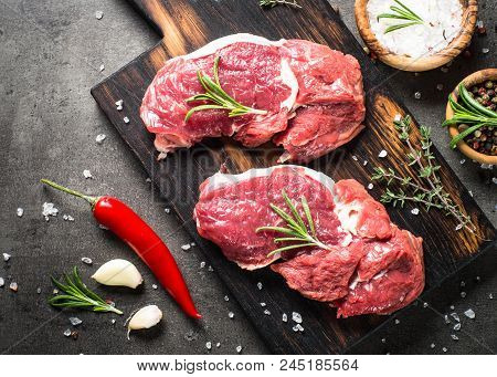 Fresh Meat. Raw Beef Steak On A Cutting Board With Rosemary And Spices On Dark Stone Table. Top View
