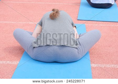 A Girl In A Gray T-shirt And Pants On A Blue Rug Is Engaged In Sports Stretching Exercises. Back Vie