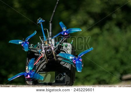 Race Drone With Blue Propellers And Transmitter With Green Background In Nature And Motors For Drone