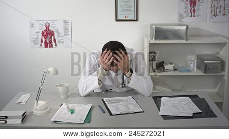 Doctor Tired And Holding His Head At Medical Cabinet, Quietly