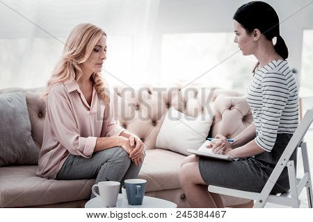 Sharing Negative Feelings. Downhearted Woman Looking Down And Keeping Hands Together While Skilled P