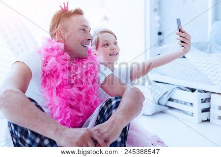 Say Cheese. Funny Mature Man Wearing A Feather Boa And A Little Crown Smiling While Sitting Next To 