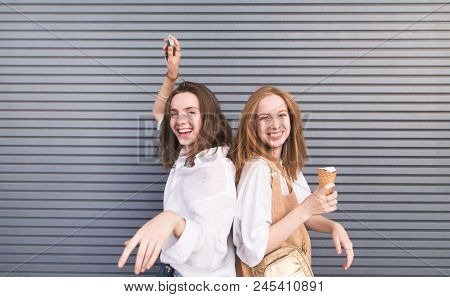 Portrait Of Two Happy Girls In Stylish Light Clothes Are Looking Into The Camera And Smiling Against