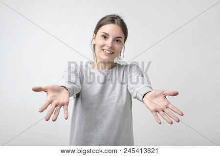 Portrait Of Attractive Smiling Teenage Girl Raised Up Arms Hands At You. She Is Dressed In Gray Simp