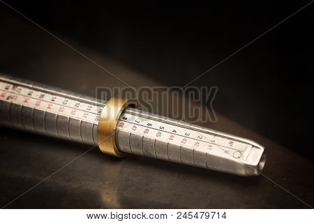 Golden Ring  On A Ring Sizer Gauge, Jeweler Sizing Tool From Steel Against A Dark Background With Co