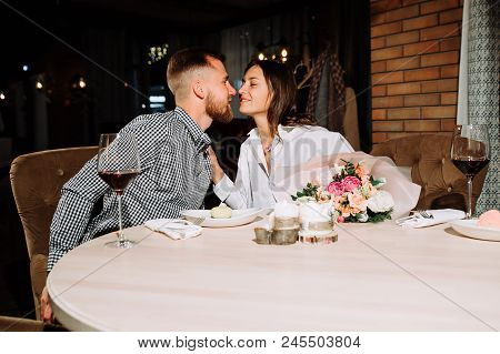 Enamored Couple Sitting In A Chair, Hug Each Other And Drinking Vine In A Cafe Or Restaurant. Two Pe