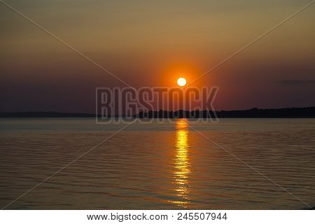 Dramatic Sunset Over The Lake. The Setting Sun And A Sunny Path On A Watery Surface Against  Red Sky