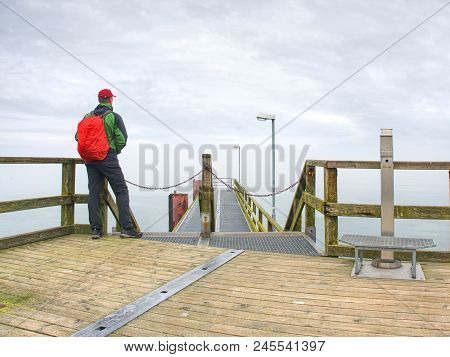 Man In Hat With Backpack Travelling, Tourist On Bridge Watch To The Sea. Lowcost  Travel