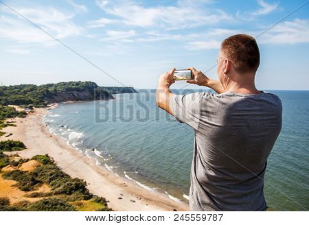 Man In A Gray T-shirt Photographing Seascape By Mobile Phone On Heat Sunny 
Sunner Day