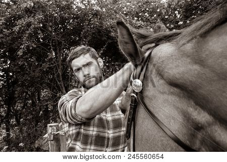 Good Looking, Hunky Cowboy Stands Next To Ranch Gate Petting And Loving His Horse